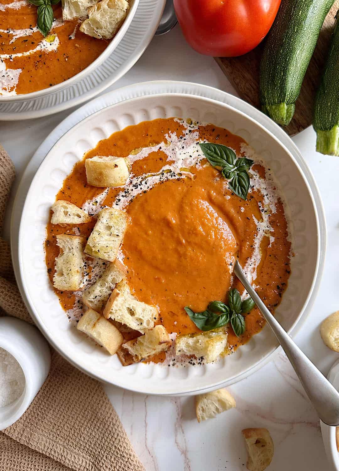 tomato zucchini soup with basil and croutons and a silver spoon