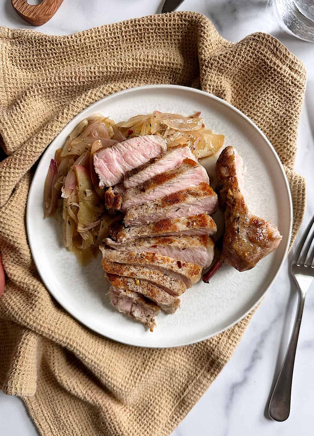 sliced pork chops with apples and shallots on white plate