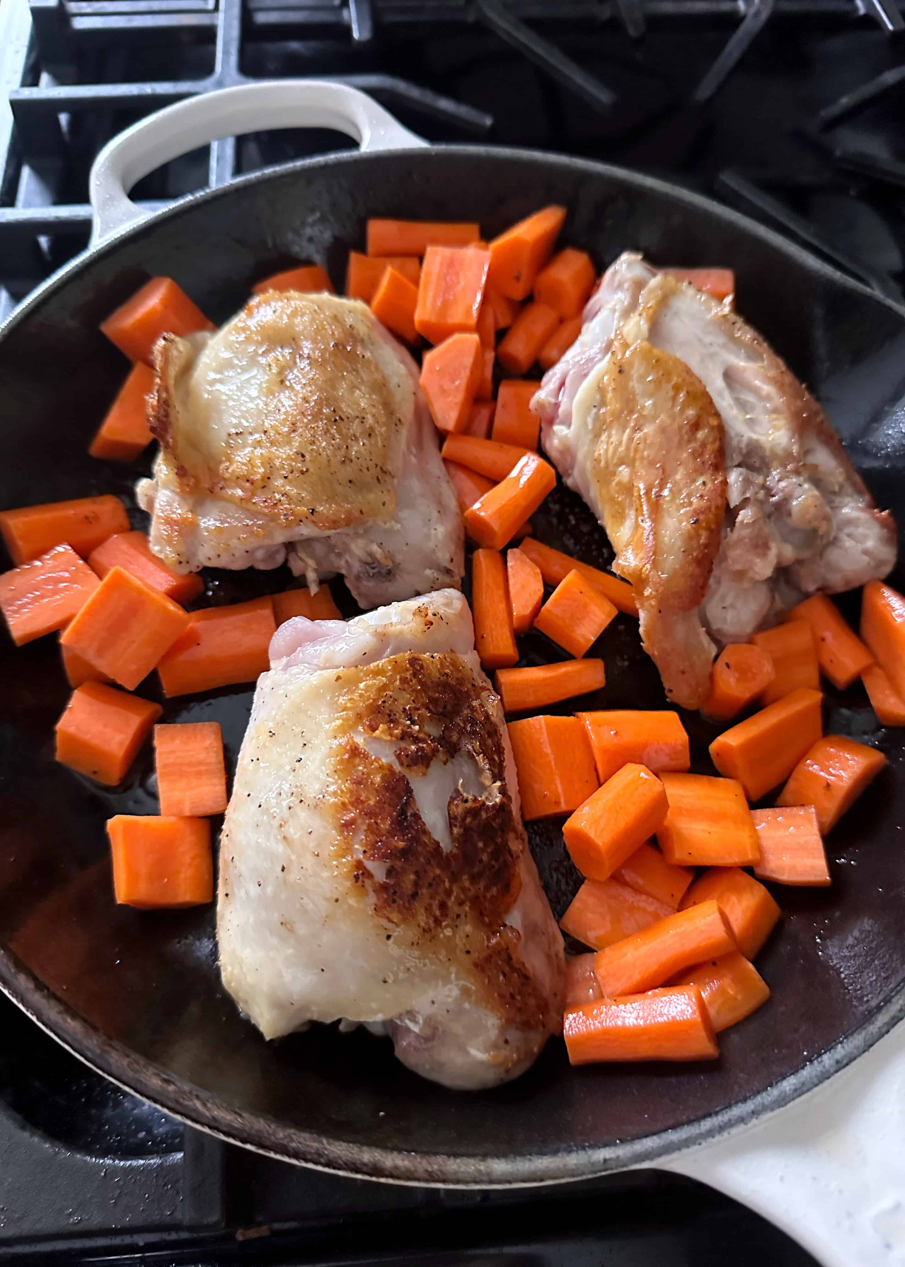 crispy chicken thighs and carrots in frying pan