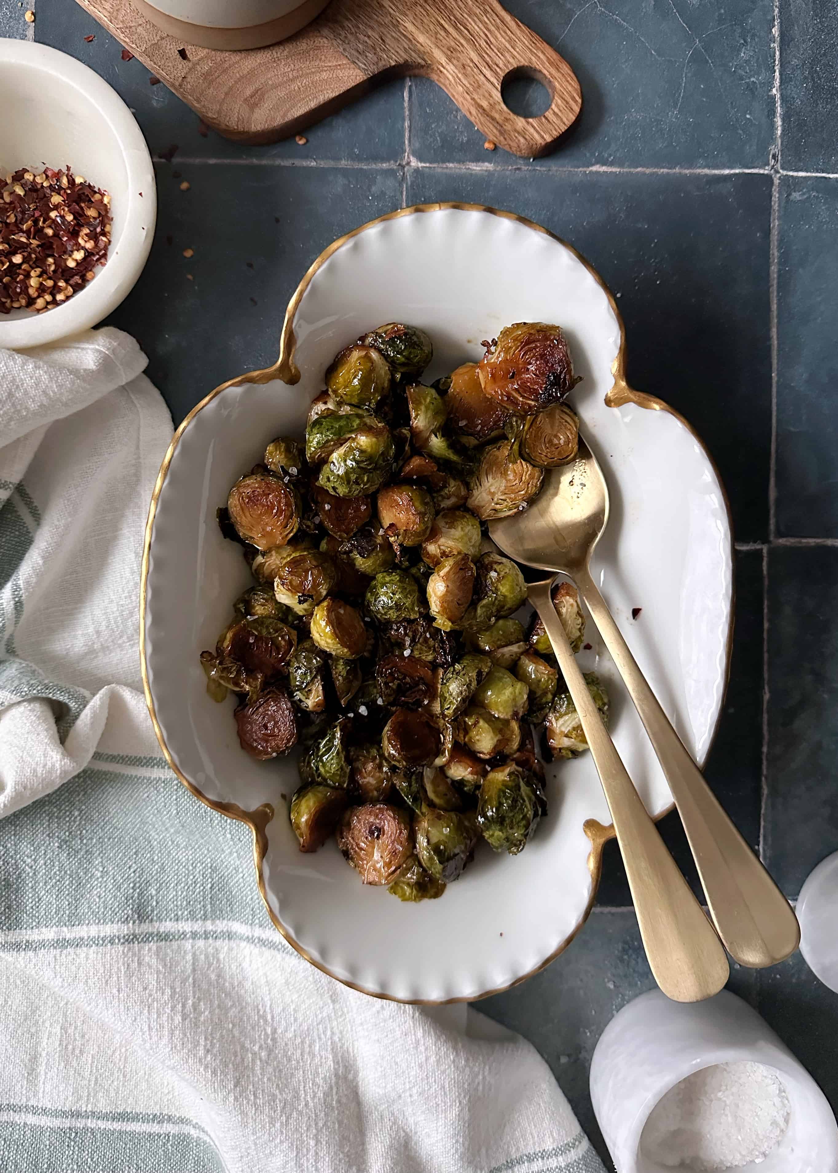 chili maple balsamic brussels sprouts with gold spoon in a white serving bowl