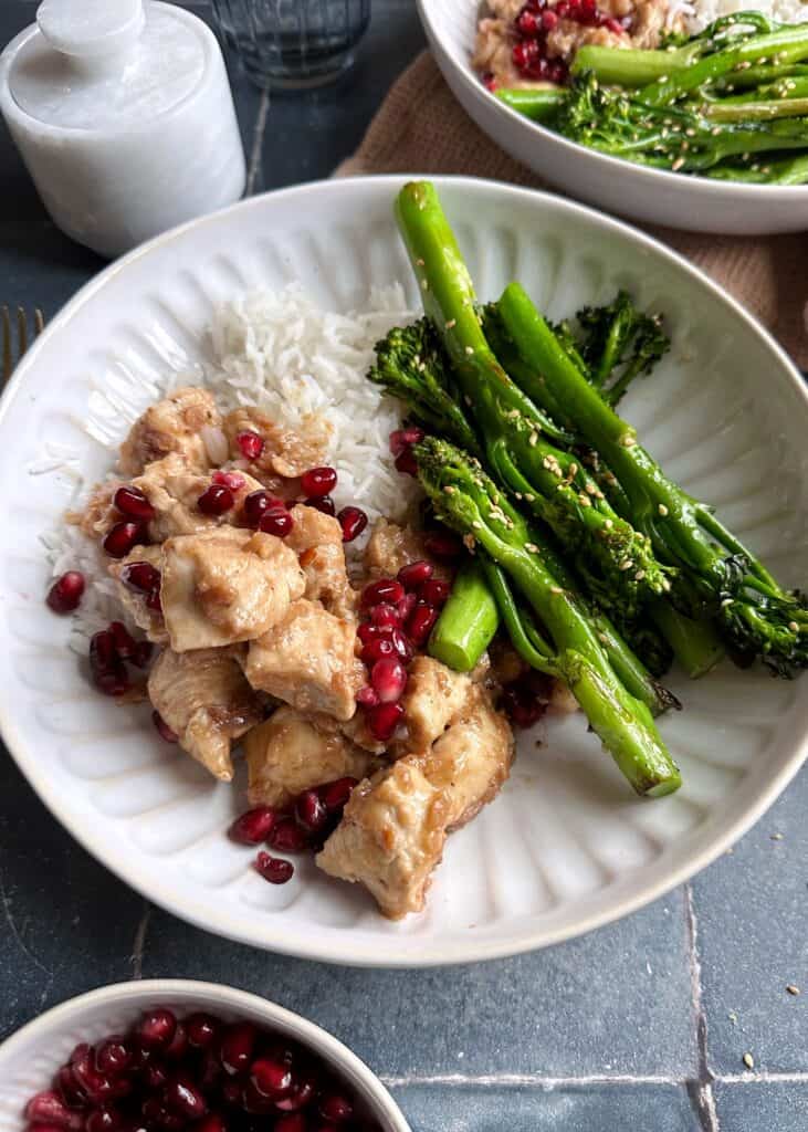 bowl of chicken with pomegranate sauce and sesame broccolini.
