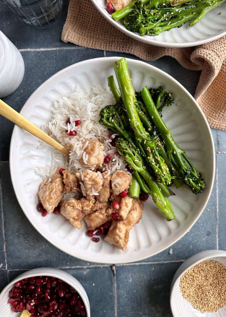 bowl of chicken with pomegranate sauce and sesame broccolini with gold fork
