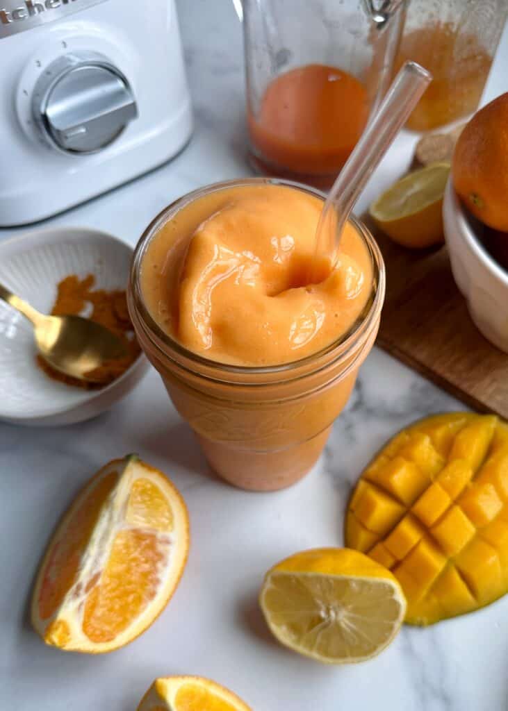 orange carrot mango smoothie in glass with a straw