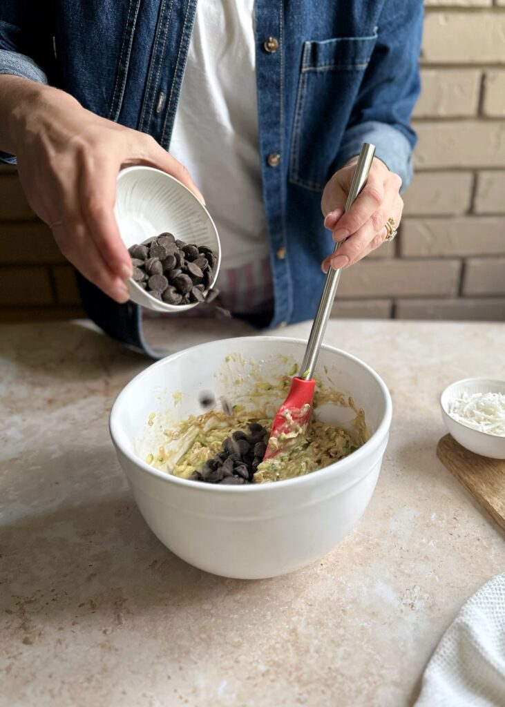 adding chocolate chips to zucchini bread batter in a white bowl