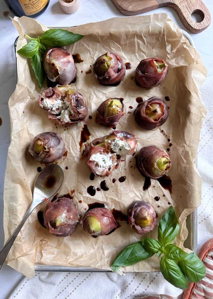 baked figs wrapped in prosciutto and stuffed with goat cheese on a tray