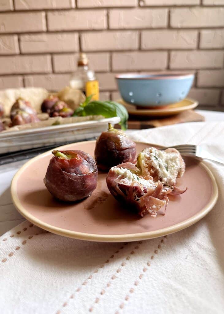 pink plate with baked figs with goat cheese prosciutto and balsamic