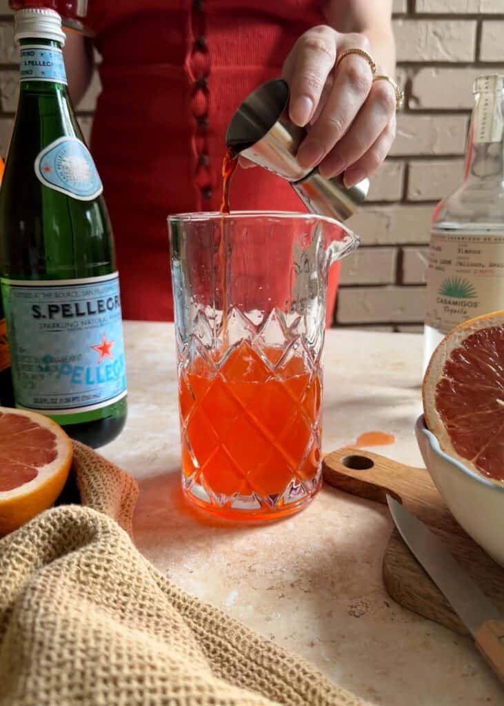 pouring aperol into a glass pitcher