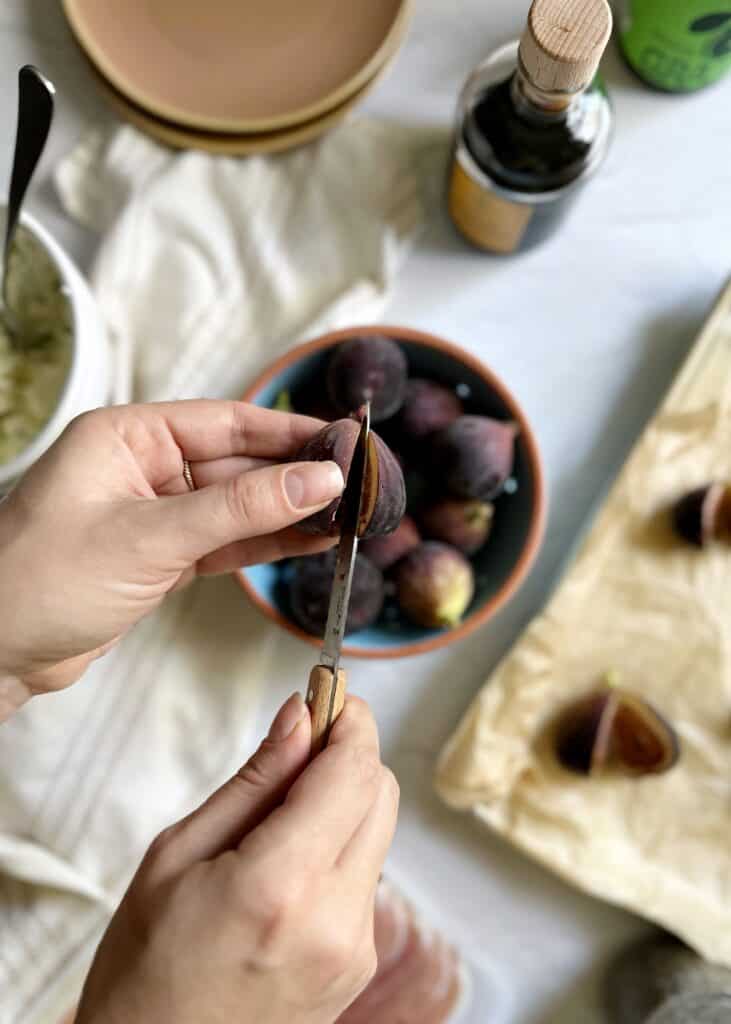 slicing a fig in half with a bowl of figs below