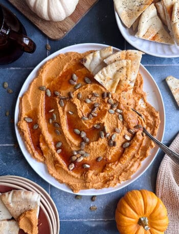 pumpkin hummus with pita chips on the side and toasted pumpkin seeds