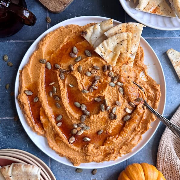 pumpkin hummus with pita chips on the side and toasted pumpkin seeds