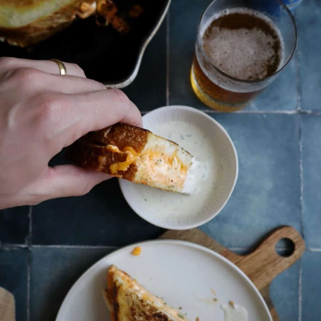 dipping buffalo chicken grilled cheese in ranch dressing with a slice on the side