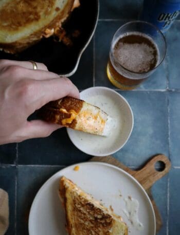 dipping buffalo chicken grilled cheese in ranch dressing with a slice on the side