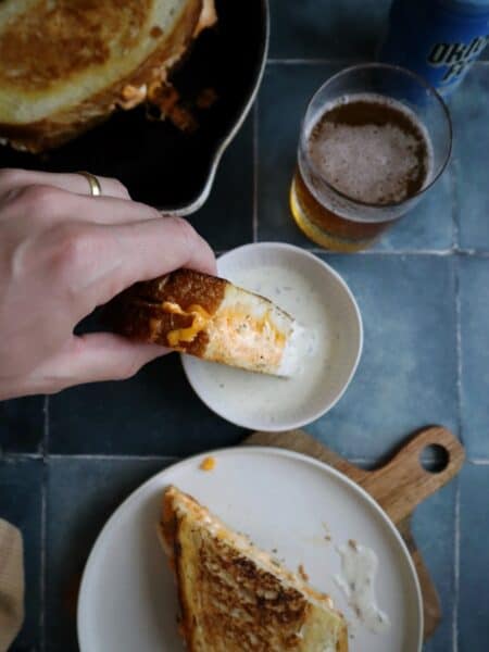 dipping buffalo chicken grilled cheese in ranch dressing with a slice on the side