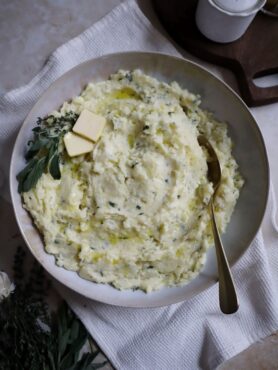 bowl of buttery garlic and herb mashed potatoes with golden spoon