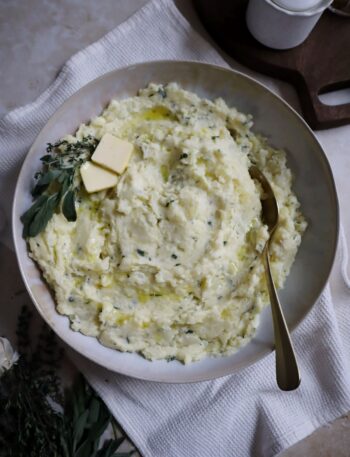 bowl of buttery garlic and herb mashed potatoes with golden spoon