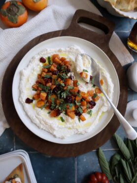 maple persimmons with ricotta cranberry and sage served on a white plate with gold spoon