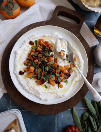 maple persimmons with ricotta cranberry and sage served on a white plate with gold spoon