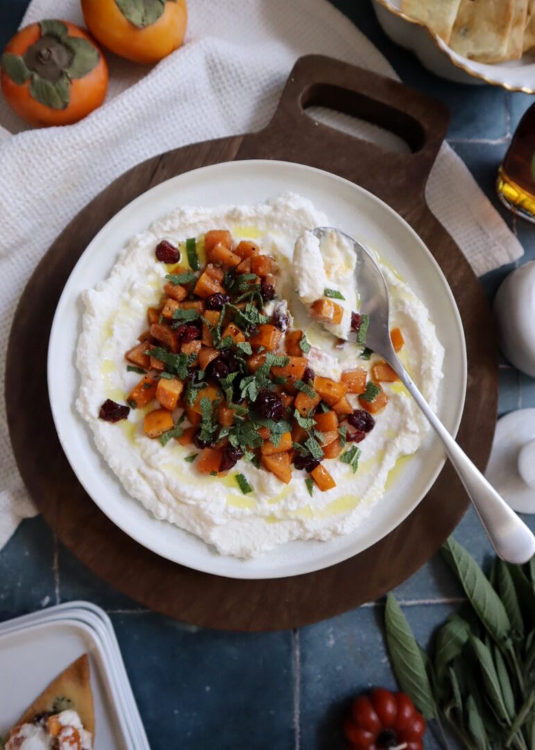 maple persimmons with ricotta cranberry and sage served on a white plate with gold spoon