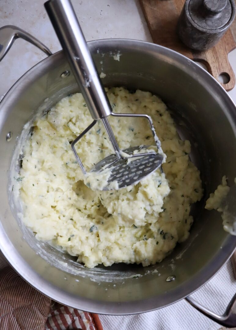 mashed potatoes in a silver pot with a potato masher