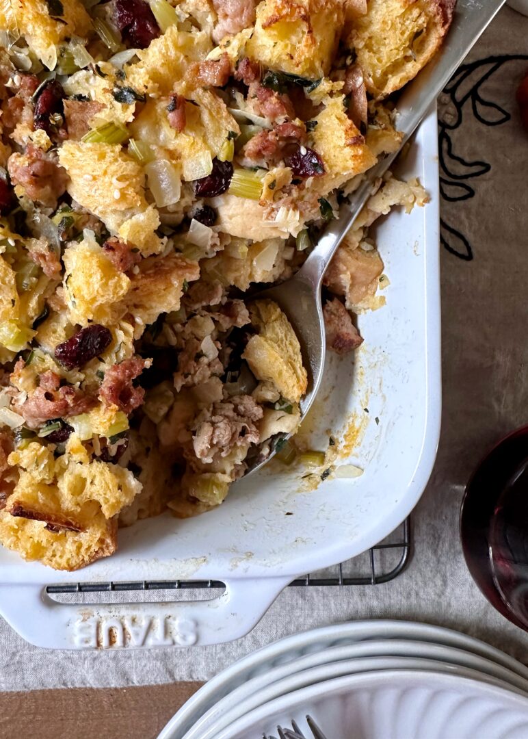 sausage and cranberry stuffing with silver serving spoon in white serving dish