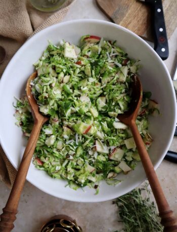 shaved brussels sprouts salad with apple manchego and almond in white bowl with wooden salad spoons