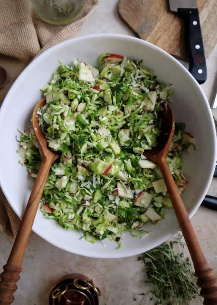 shaved brussels sprouts salad with apple manchego and almond in white bowl with wooden salad spoons