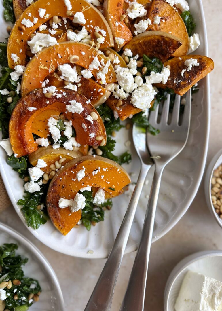 butternut squash kale salad feta and pine nuts with silver serving spoons