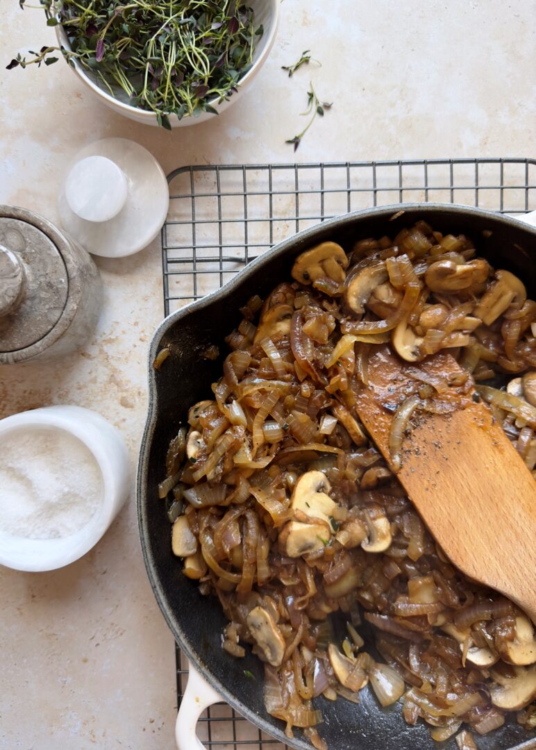 caramelized onions and mushrooms with fresh thyme in a cast iron pan with a wooden spatula