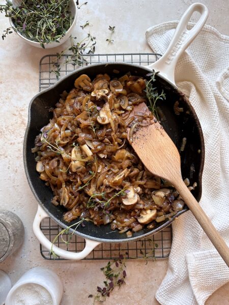 caramelized onions and mushrooms with fresh thyme in cast iron skillet with wooden spatula