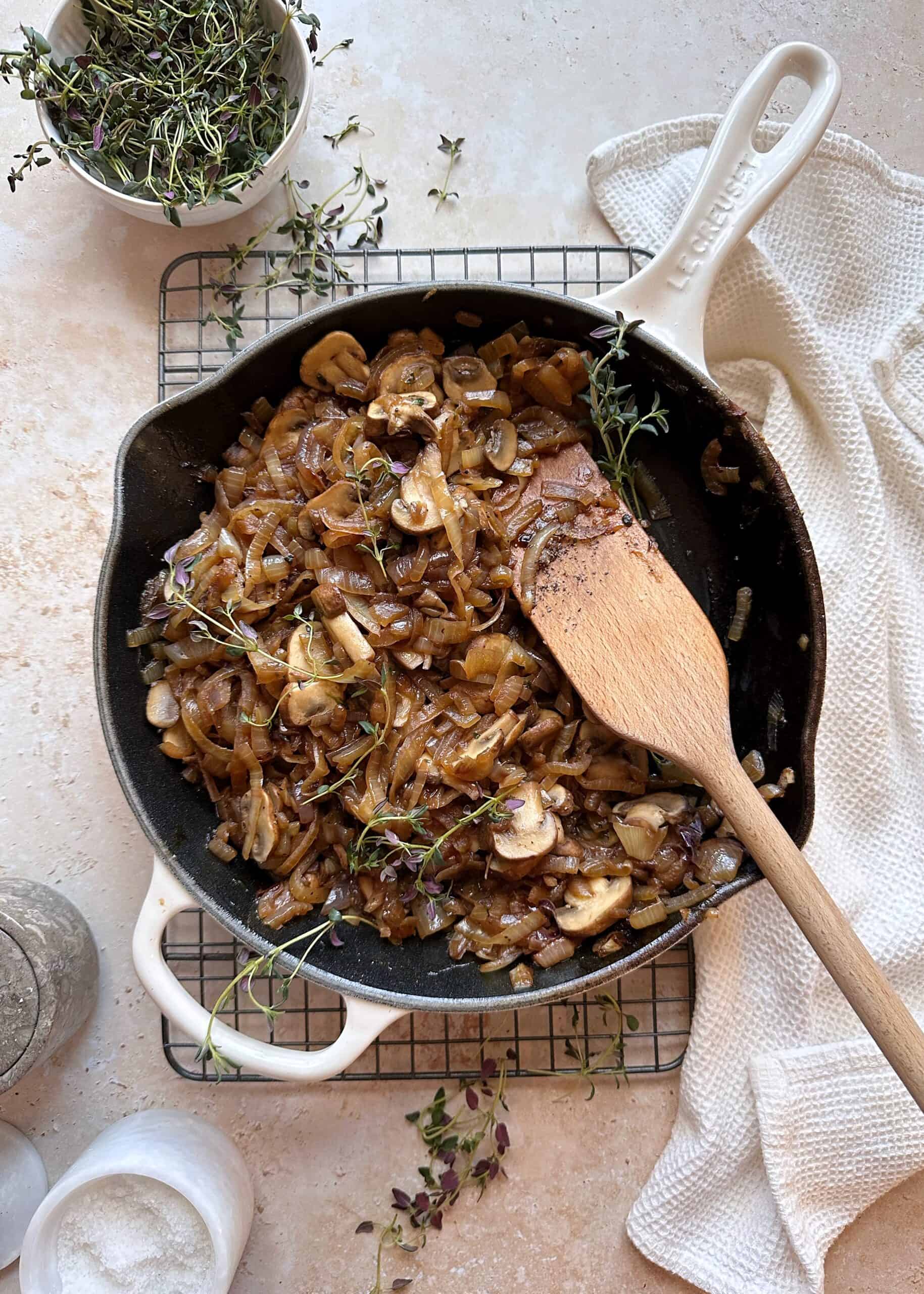 caramelized onions and mushrooms with fresh thyme in cast iron skillet with wooden spatula