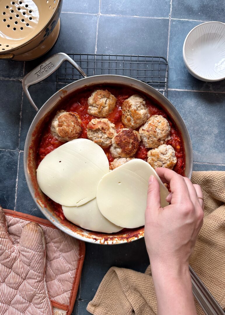 layering slices of cheese over chicken meatballs in marinara before baking