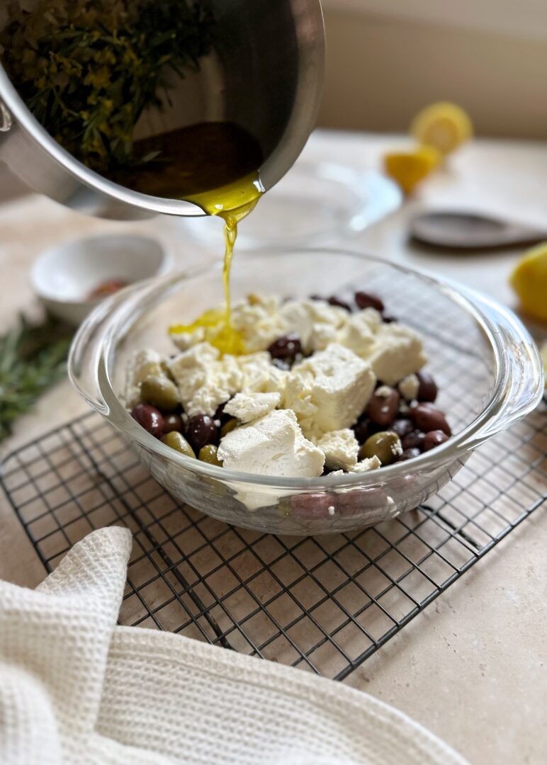 pouring marinade over feta and olives in a glass bowl