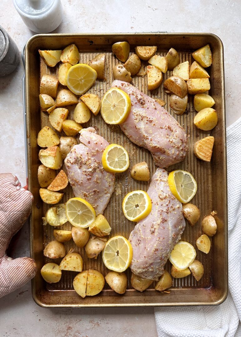 chicken nestled into parbaked potatoes on a baking tray