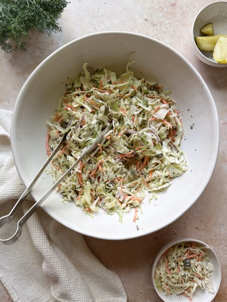 dill pickle coleslaw in white bowl with silver tongs