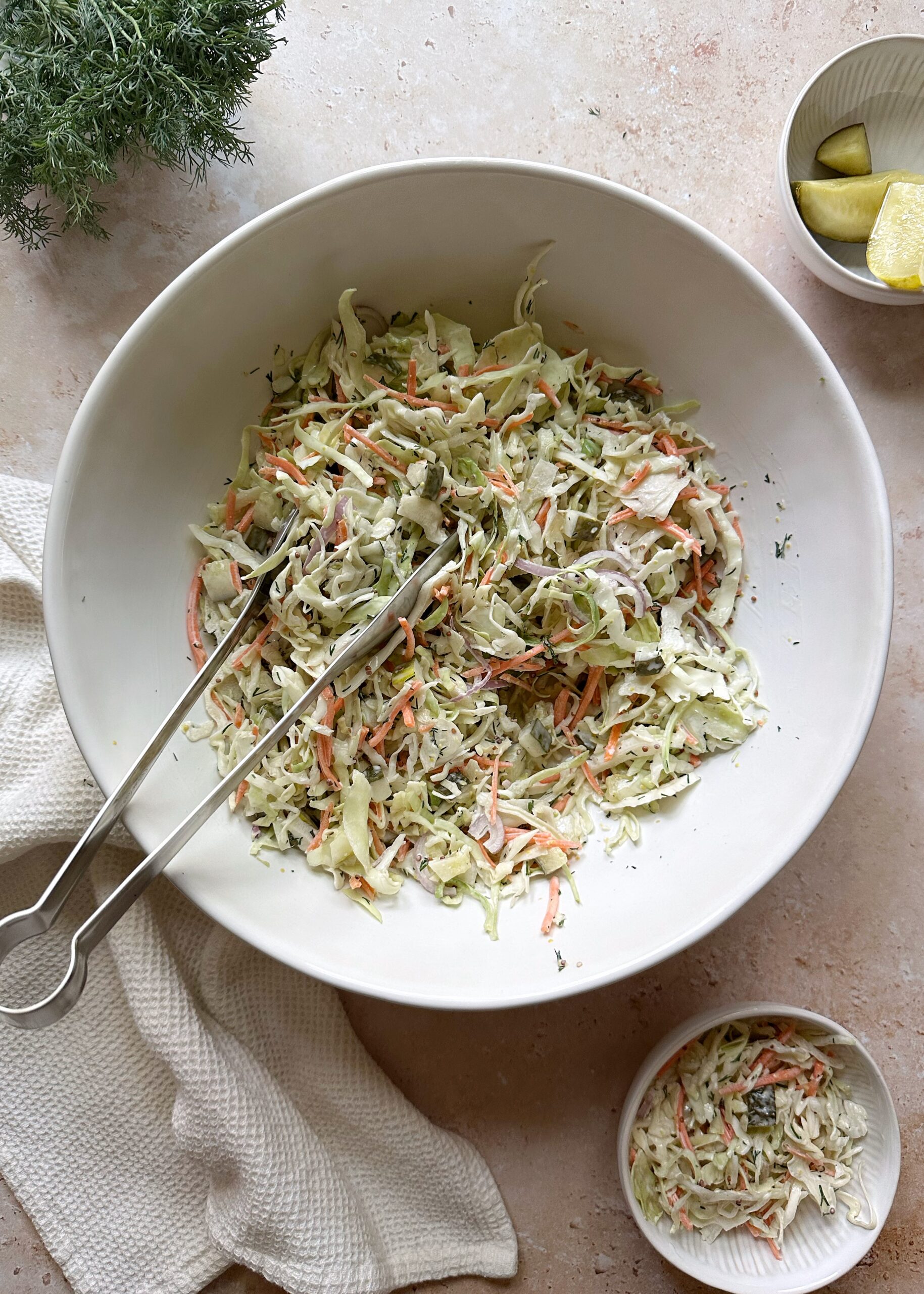 dill pickle coleslaw in white bowl with silver tongs