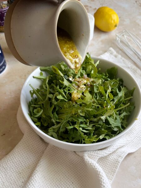 pouring lemon and mustard vinaigrette over green salad