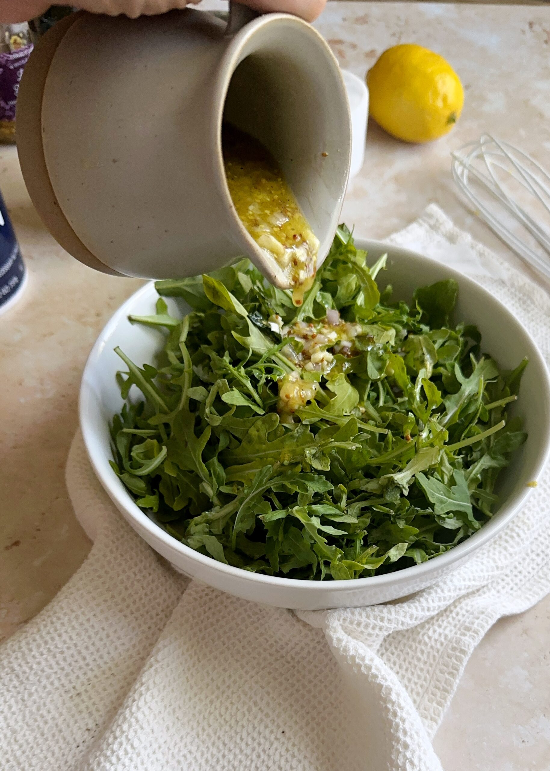 pouring lemon and mustard vinaigrette over green salad