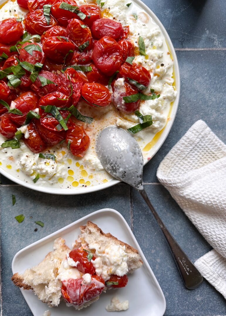 burst grape tomatoes with burrata and fresh basil on a tray with a silver spoon