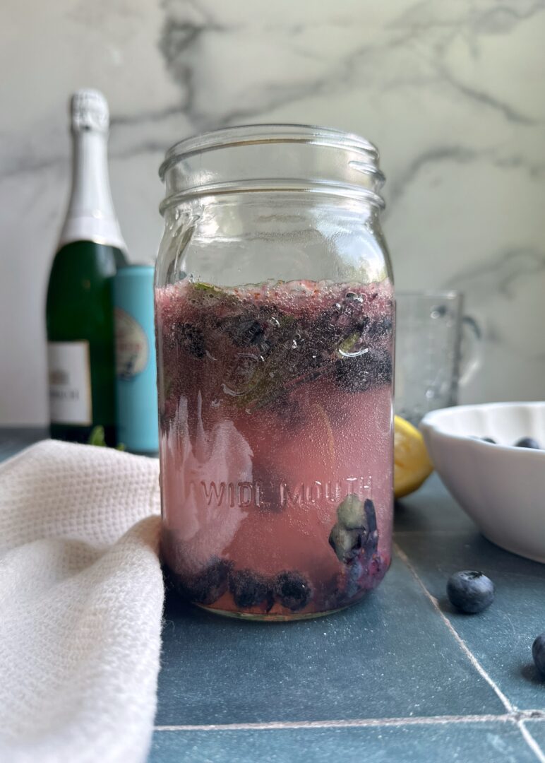 glass jar of smashed blueberries with vodka and ginger beer