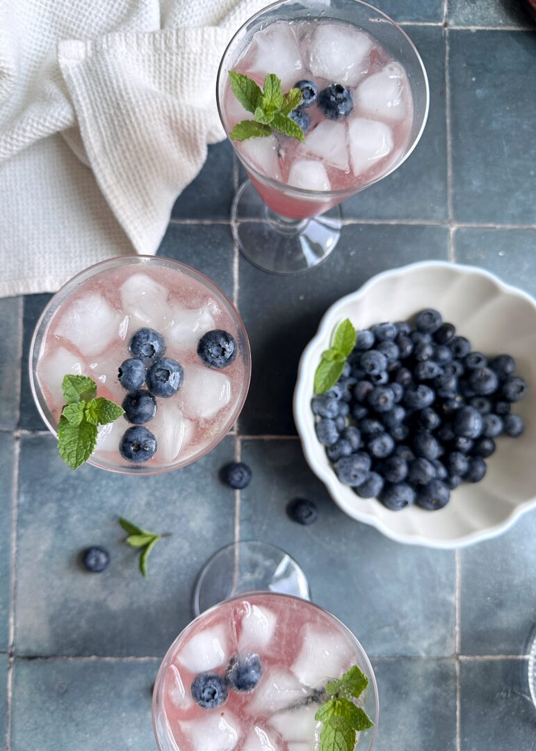 glasses of blueberry champagne mules with bowl of blueberries on the side