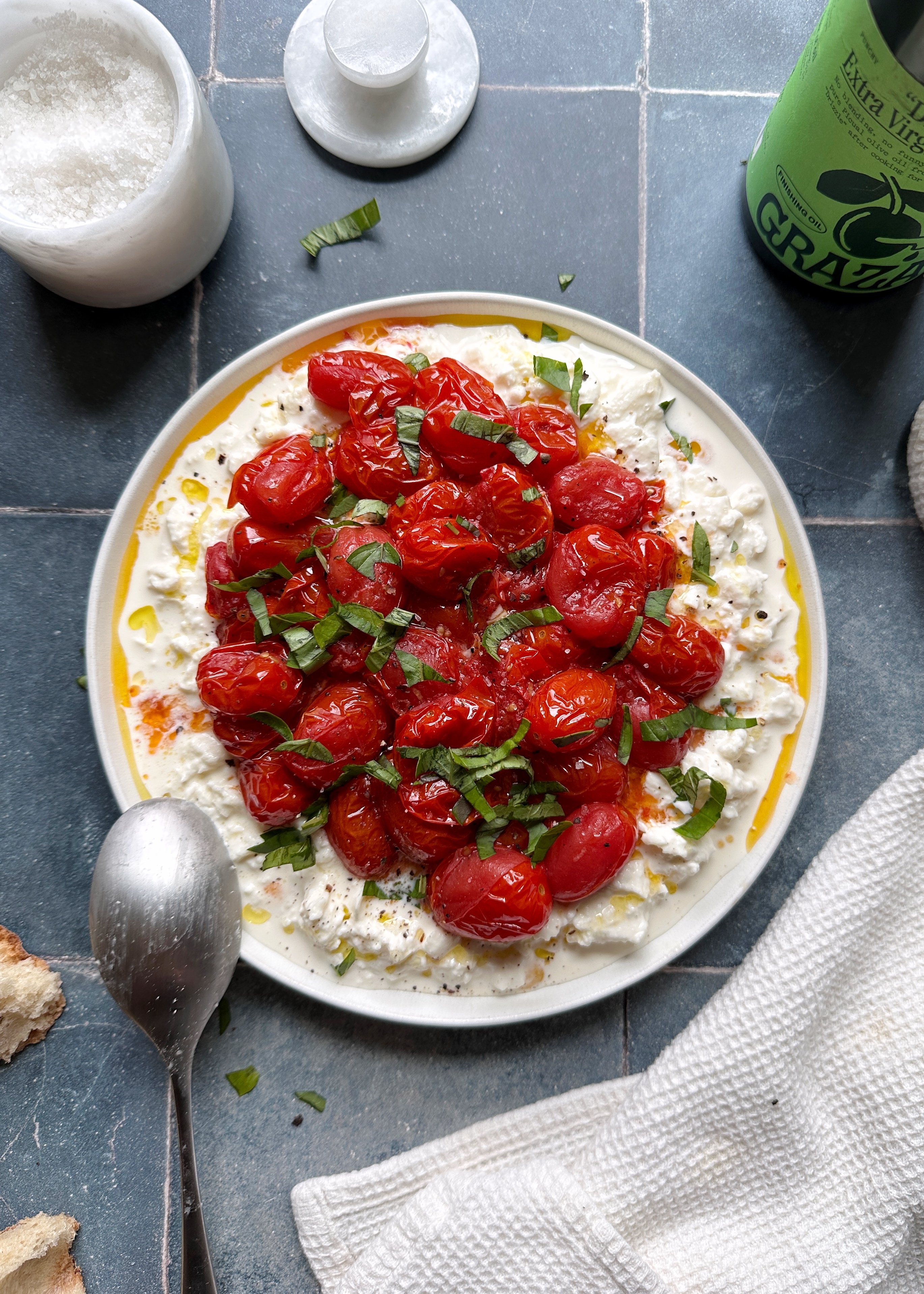 plate of burst grape tomatoes with burrata cheese and fresh basil