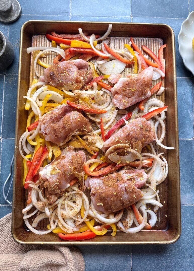 Cajun chicken thighs and peppers on a baking sheet