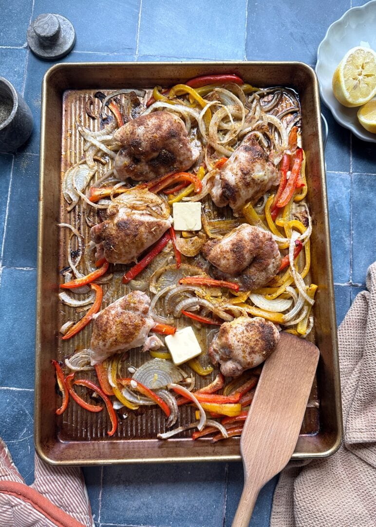 baking sheet with Cajun chicken thighs peppers and onions