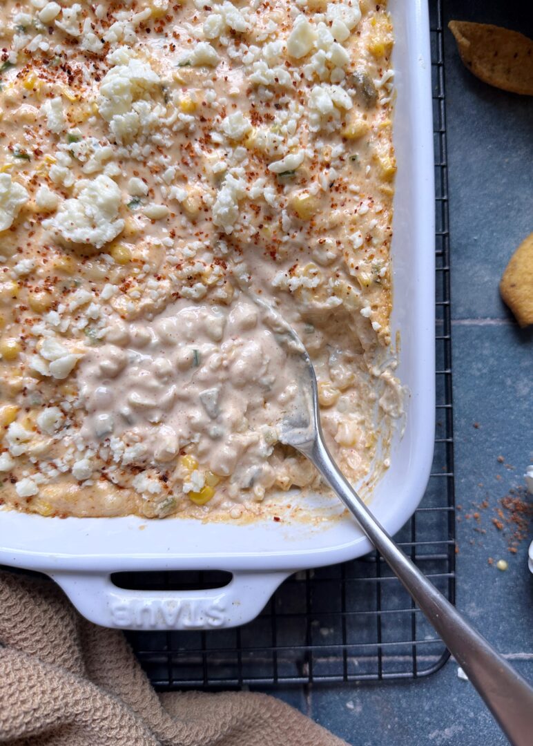 casserole dish of creamy elote dip with a silver spoon