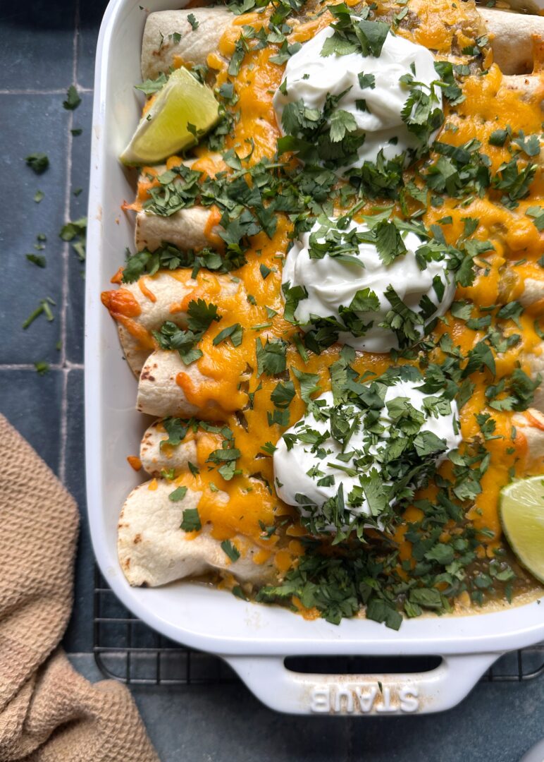 casserole dish of green chile chicken enchiladas with sour cream and cilantro garnish