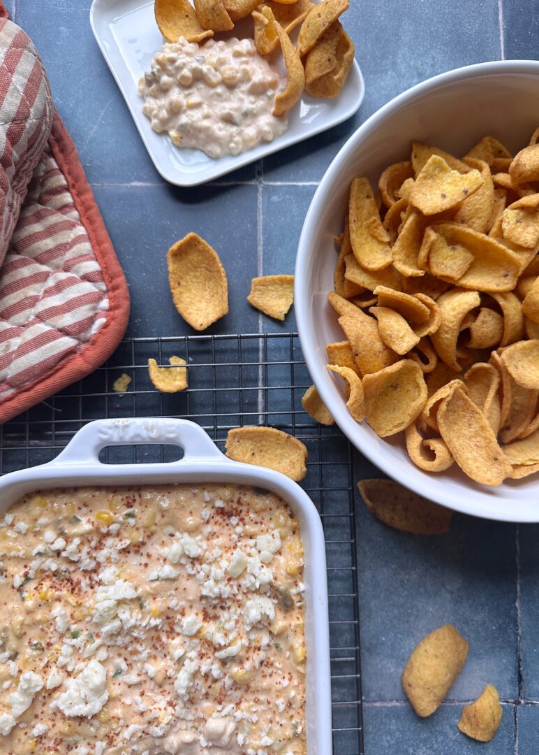 creamy elote dip in a casserole dish with a side of corn chips