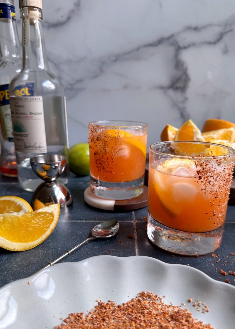 glasses of orange aperol margaritas with tajin rim and orange slices