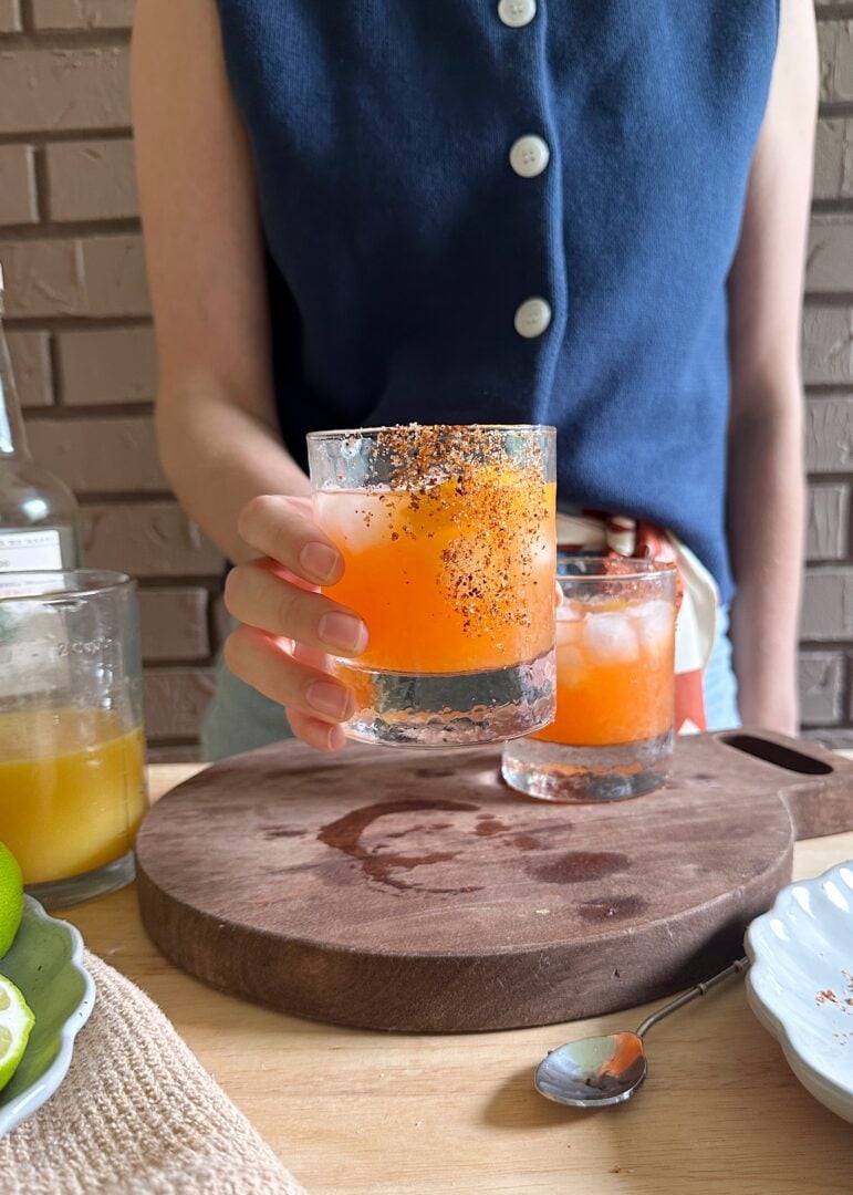 holding a glass of orange aperol margarita