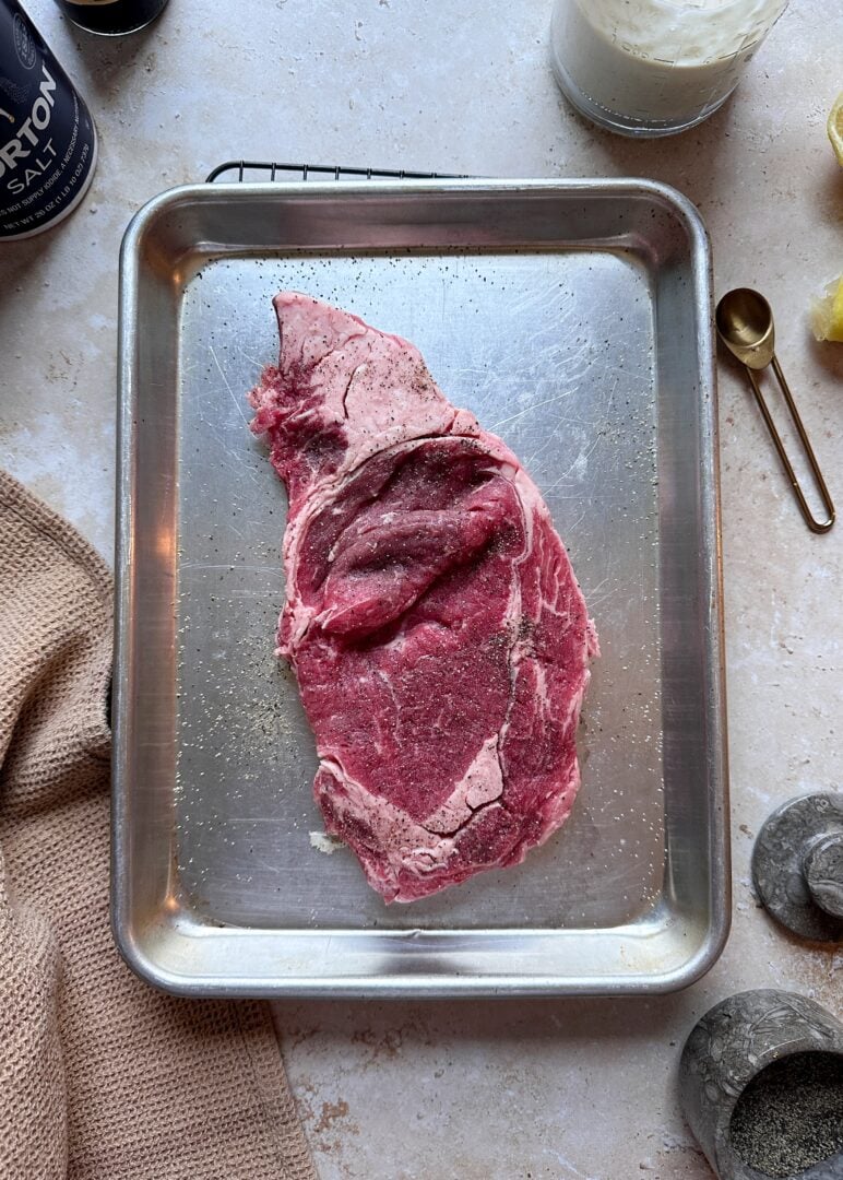 seasoned ribeye steak on silver tray before grilling