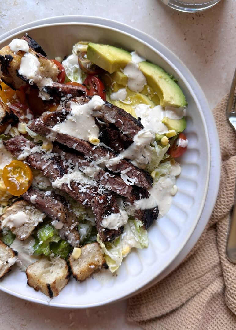 serving of grilled steak caesar salad with tomatoes corn and avocado